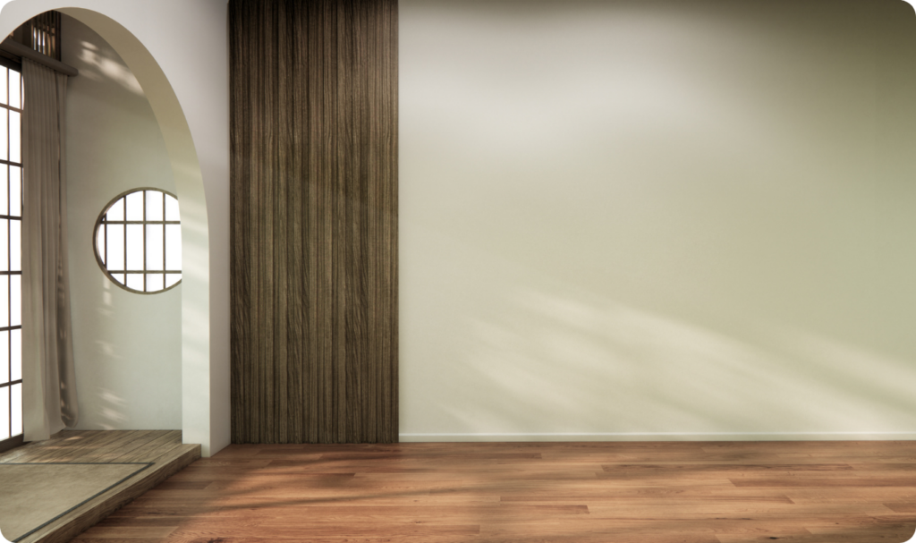 Interior de um ambiente vazio com estilo minimalista e tons neutros. À direita, uma parede lisa pintada em bege claro recebe iluminação natural difusa. À esquerda, um painel vertical de ripas de madeira escura e uma abertura em arco que dá acesso a outro cômodo com piso de madeira, janela circular e cortinas claras. O piso principal é de réguas de madeira em tom médio.